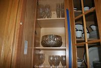 Wood cabinet shelf with multiple glasses and a clear crystal bowl.