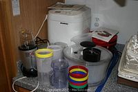 Photo of Magic Bullet blender with multiple cups and rings, salad spinner, and red waffle iron and mini donut maker on counter