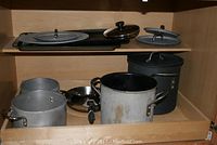 Pots, pans, and cookie sheets stored on shelf showing varying sizes and types with lids