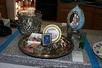 Photo of various decorative items on a kitchen counter including an egg carousel music box, frog figurine, small picture frames, metal tray, metal grape ice bucket, green glass vase, and decorative boxes.