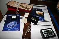 Overview of jewelry pieces on table including pearl necklace, gemstone bracelet, brooch, earrings, pendant chains, and boxes containing semi-precious stones and invoices.