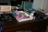 Wide view of a dresser top displaying multiple trays, boxes, and stands filled with assorted costume jewelry including necklaces, bracelets, and earrings.