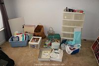 Wide shot showing multiple plastic storage bins, boxes, and bags containing arts and crafts materials on carpeted floor.
