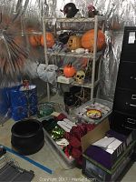 Photo showing shelving unit containing pumpkins, masks, skull decoration, ribbons, Christmas stocking and ornaments boxes on floor