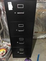 Black metal 4-drawer filing cabinet with handles and label holders, front view.