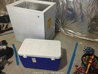 Photo of the GE chest freezer and the blue portable cooler side by side on a concrete floor, showing overall external condition and size comparison.