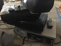 Top view showing a black boom box with cassette player placed on top of two stacked audio/video devices with remote controls on the side.