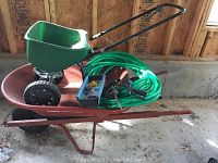 Photo of all items in lot including wheelbarrow, spreader, coiled hose with spray nozzle and box of packets.