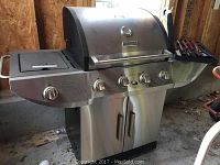 Front view of stainless steel Kenmore propane grill showing five control knobs, side burner and storage cabinet