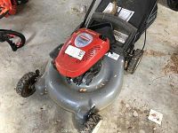 Full view of Craftsman gas push lawnmower showing red engine housing, gray deck, and wheels on concrete floor with visible wear and damage.