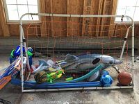 White metal framed soccer goal with attached orange net, filled with various inflatable beach toys and balls including a large silver dolphin float and two inflatable balls.