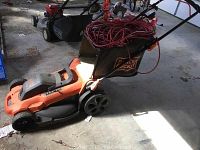 Side view of the orange and black Black and Decker electric lawnmower with grass catcher bag and extension cord on top.