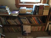 Bookshelves and table stacked with various paperback and hardcover books in used condition.