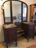 Full front view of the vintage vanity showing the three-part folding mirror, the two cabinetry sides with drawers, and the central bench area.