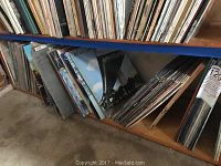 Various vinyl records arranged vertically on wooden shelves. Assorted album artwork visible including graphic and photographic cover art.