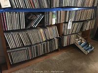 Wide view of wooden bookshelf filled with multiple rows of audio CDs showing typical jewel cases and a box set on the floor.