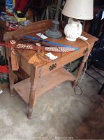 Full view of wood vanity table with drawer, lower shelf, and various items placed on top including lamps and decorative pieces.
