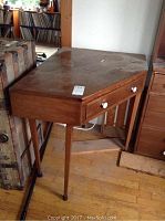 Full view of wooden corner desk showing the surface scratches, single drawer with white knobs, four legs, and general wear.
