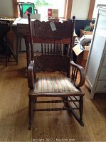 Front view of the wooden rocking chair showing carved details on backrest and upholstered striped seat.