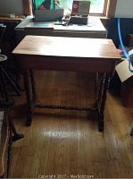 Full view of the wooden side table showing turned legs and stretcher bar on hardwood floor.