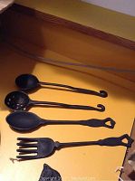 Four cast iron kitchen utensils with curved handles on flat yellow surface