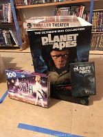 Large box set of Planet Of The Apes DVD Ultimate Collection with bold ape face on front. Also includes 100 Greatest Sci-Fi Classics 24-disc set in a colorful box with sci-fi theme. Smaller Planet Of The Apes DVD case in front.