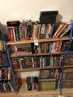 Three-tier wooden shelf holding assorted DVDs and blank DVD cases.
