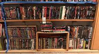 Full shelving unit with three rows of DVDs and a small crate in front