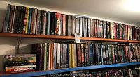 Photo showing a wide variety of DVDs on a wooden shelf, various movie DVDs including titles in multiple genres.