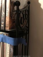 Right-side view of black metal rack showing scrollwork detail and DVDs on shelves