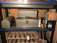 The full shelf with metal Craftsman toolbox open showing various hand tools inside, a cardboard box likely containing the Sears bench vise, and other small items on the shelf.