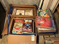 Overhead view of two wooden crates strapped together containing open cardboard boxes filled with assorted comic books, magazines and sketchbooks.