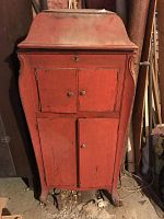 Front view of red painted antique Victrola cabinet phonograph showing two cabinet doors with missing knob and keyhole.