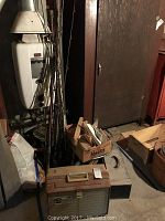 Multiple vintage fishing rods stored upright in a box and leaning against a wall, surrounded by various boxes and supplies in a basement or garage space.