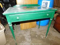 Front angle of vintage green metal desk showing drawer and wear on legs and surface