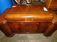 Front view of the closed wooden cedar chest showing the polished top and curved side pillars.