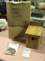 Two wooden wren birdhouses next to their labeled boxes, along with mounting hardware in plastic bags and auction tags.