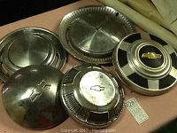 Five vintage Chevrolet hubcaps arranged on a surface, showing front side with varying designs and wear.