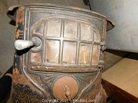 Close-up of the front door of the antique cast iron stove showing the multi-paneled door, white handle, and rusted surface.
