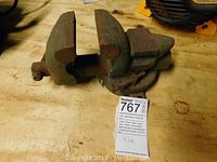 Heavy duty metal bench vice positioned on a wooden surface, showing the front and side angles with visible wear and rust.