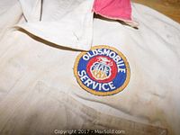 Close-up of chest patch with Oldsmobile Service logo on white jumpsuit with red collar
