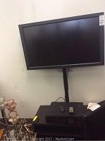 Full view of the black 40-inch NEC MultiSync LCD 410 monitor mounted on a wall mount above a black TV stand holding the VCR and remotes.