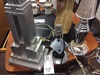 Wider view showing three metal table lamps: Empire State Building replica, dice-shaped lamp, and chrome lamp with clear glass shade; power cords visible