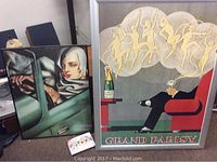 Three framed art prints on floor including large 'Grand Parisy' print with broken glass, a print with a person in a car, and a colorful abstract print