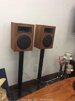 Pair of Realistic brand standing speakers on black stands, shown against a white wall with power cords visible.