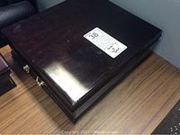 Closed wooden jewellery box with brass handles and surface wear and scratches.