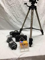 Nikon F-401 and N2020 cameras, flash, film rolls, and Velbon GX-440 tripod arranged on white background