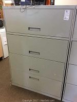 Front view of a grey metal 4-drawer file cabinet with recessed handles and lock on top center, showing signs of wear.