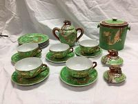 Full view of the green and gold Mikori bone china tea set with cups, saucers, side plates, lidded container, and ice bucket showing the Asian dragon motif decoration.