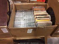Wide view of a large cardboard box filled with CDs and 45 RPM vinyl records in paper sleeves
